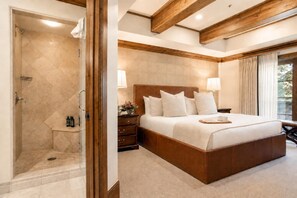 Un dormitorio con una cama grande, una mesita de noche, una ducha y una ventana con cortinas.
