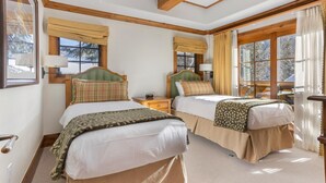 Ein Hotelzimmer mit zwei Betten, Holzbalken an der Decke, großen Fenstern mit Vorhängen und Blick auf Bäume.