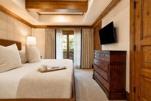 A hotel room with a bed, a dresser, a flat-screen TV, and a window with curtains.