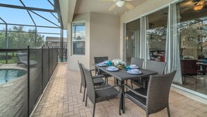 Veranda coperta con tavolo imbandito per mangiare, sedie, ventilatore a soffitto e vista su una piscina.