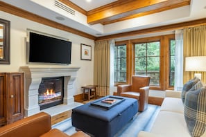 A living room with a fireplace, a television mounted above it, and a large window with curtains. - Willows 101 | Luxury 2BR Vail Village (Vail)