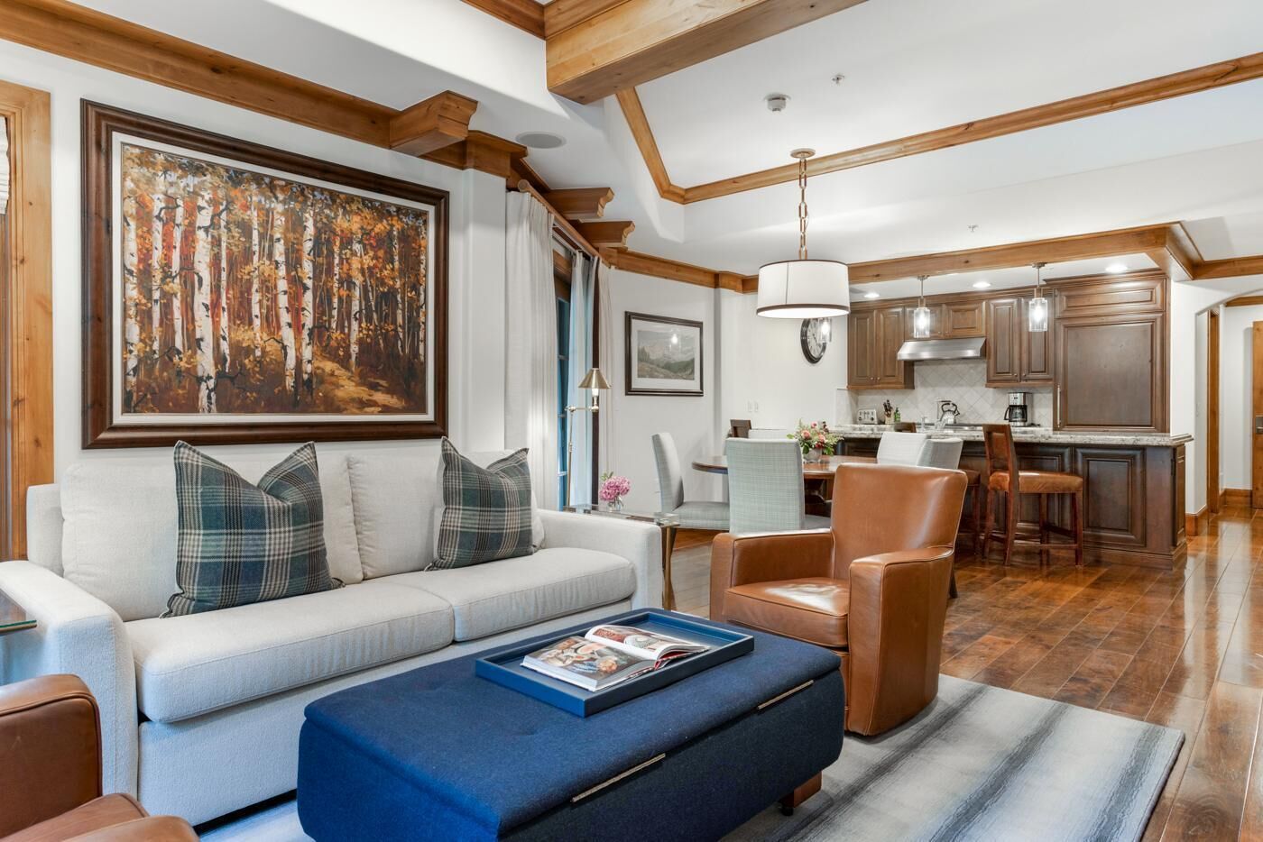 Un salon moderne avec un canapé, des fauteuils et une table basse. On aperçoit à l’arrière-plan un coin repas avec une table et des chaises.