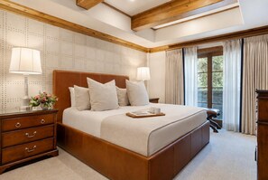 Une chambre d’hôtel avec un grand lit, une tête de lit en bois, deux lampes de chevet, une table de chevet, une commode et une fenêtre avec des rideaux.