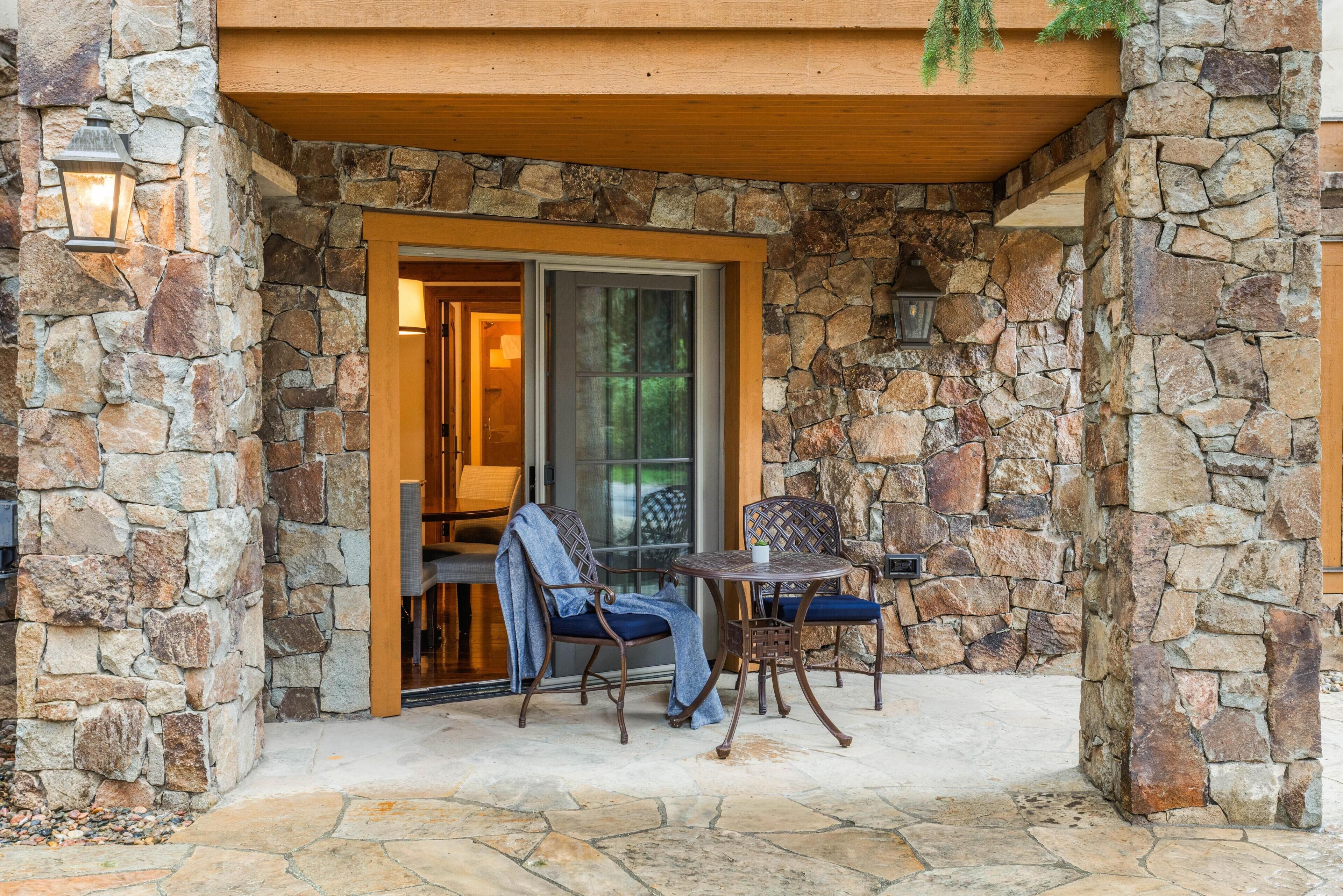 Une façade en pierre avec une porte en bois, deux chaises et une table.