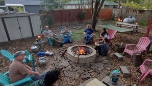 A backyard gathering with a fire pit, outdoor seating, and a wooden table with food and drinks. - Tawakoni, lake front House /jacuzzi/fire pit. (Wills Point)