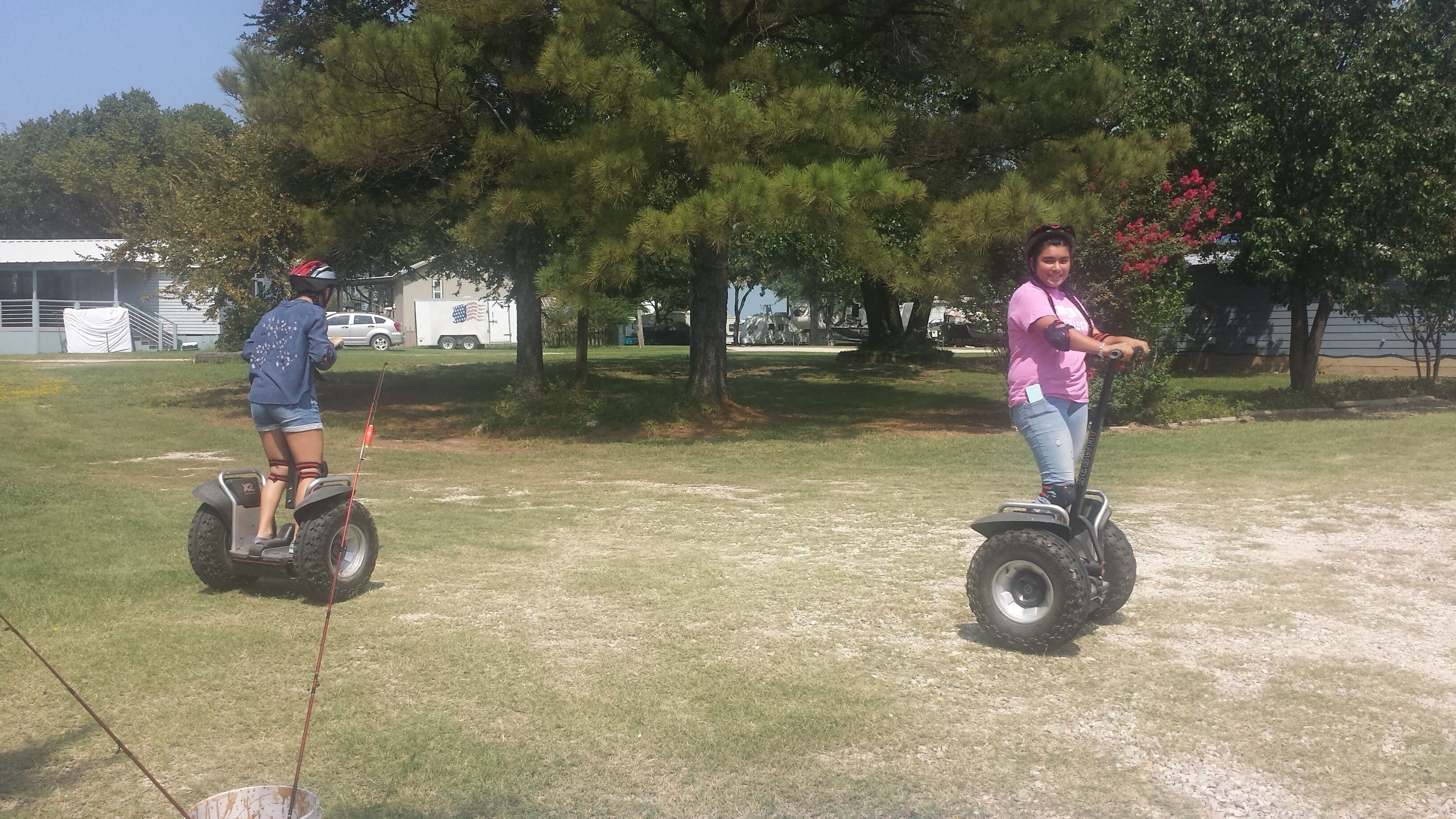 Two people on segways in a grassy area with trees and a building in the background.