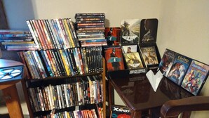 A room with a wooden bookshelf filled with DVDs and Blu-rays, a small table with a few items on it, and a chair. - Tawakoni, lake front House /jacuzzi/fire pit. (Wills Point)