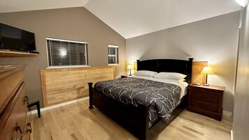 Ein Schlafzimmer mit Holz-Kopfteil, einem Bett mit gemustertem Überwurf, zwei Nachttischlampen und einem Fernseher auf einem Regal über dem Bett.