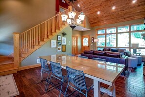 A spacious living area with a large wooden staircase, a dining table with chairs, and a leather sofa.