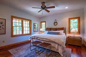 A bedroom with a bed, bedside tables, a ceiling fan, and large windows.