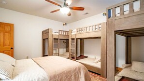 Una habitación con literas, ventilador de techo, una puerta y una cama con colcha.