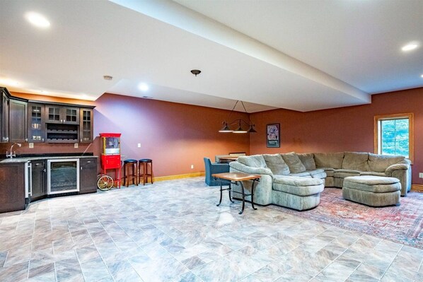 A spacious living area with a large sectional sofa, a kitchen with dark cabinets, and a red bar cart.