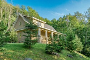 A two-story house with a porch, surrounded by a forested landscape.