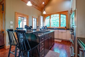 A kitchen with a central island, bar stools, wooden cabinets, and large windows.
