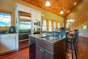 A kitchen with a stainless steel refrigerator, oven, and microwave, a granite countertop, and a wooden staircase.