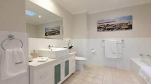 A modern bathroom with a large mirror, a sink, a toilet, and a bathtub. There are towels and a potted plant on the counter. - Shore To Please - comfort, cafes and beaches (Kiama)