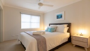 A neatly arranged bedroom with a bed, bedside table, and a ceiling fan. - Shore To Please - comfort, cafes and beaches (Kiama)