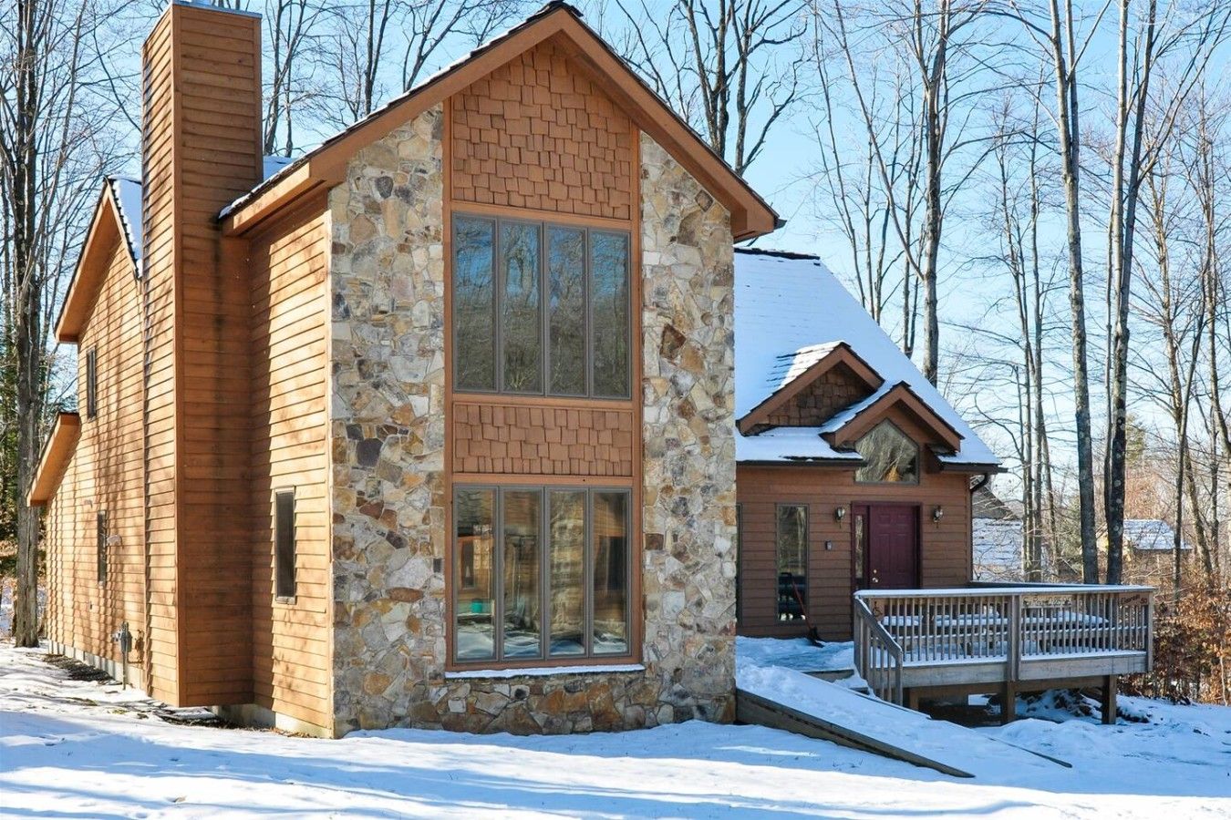 A two-story log cabin with a stone facade, large windows, and a snow-covered deck.