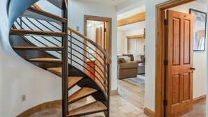 A spiral staircase with wooden steps and metal railings, leading to a living area with a sofa and a wooden door. - Riva Ridge 735 | 4BR Vail Village (Vail)