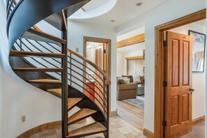 Eine Wendeltreppe mit Holzstufen und Metallgeländern führt zu einem Wohnbereich mit einer Couch und einer Holztür.
