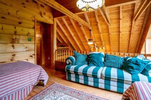 A cozy log cabin interior with a checkered sofa, a striped bed, and a wooden staircase.