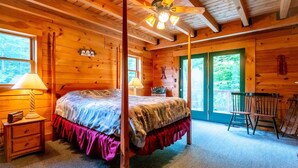 Quarto de cabana de madeira com cama de dossel, mesa de cabeceira, abajur e uma cadeira.