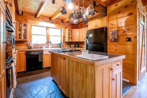 Eine Holzhütte mit einer Kücheninsel, einem Geschirrspüler, einem Kühlschrank und hängenden Töpfen.