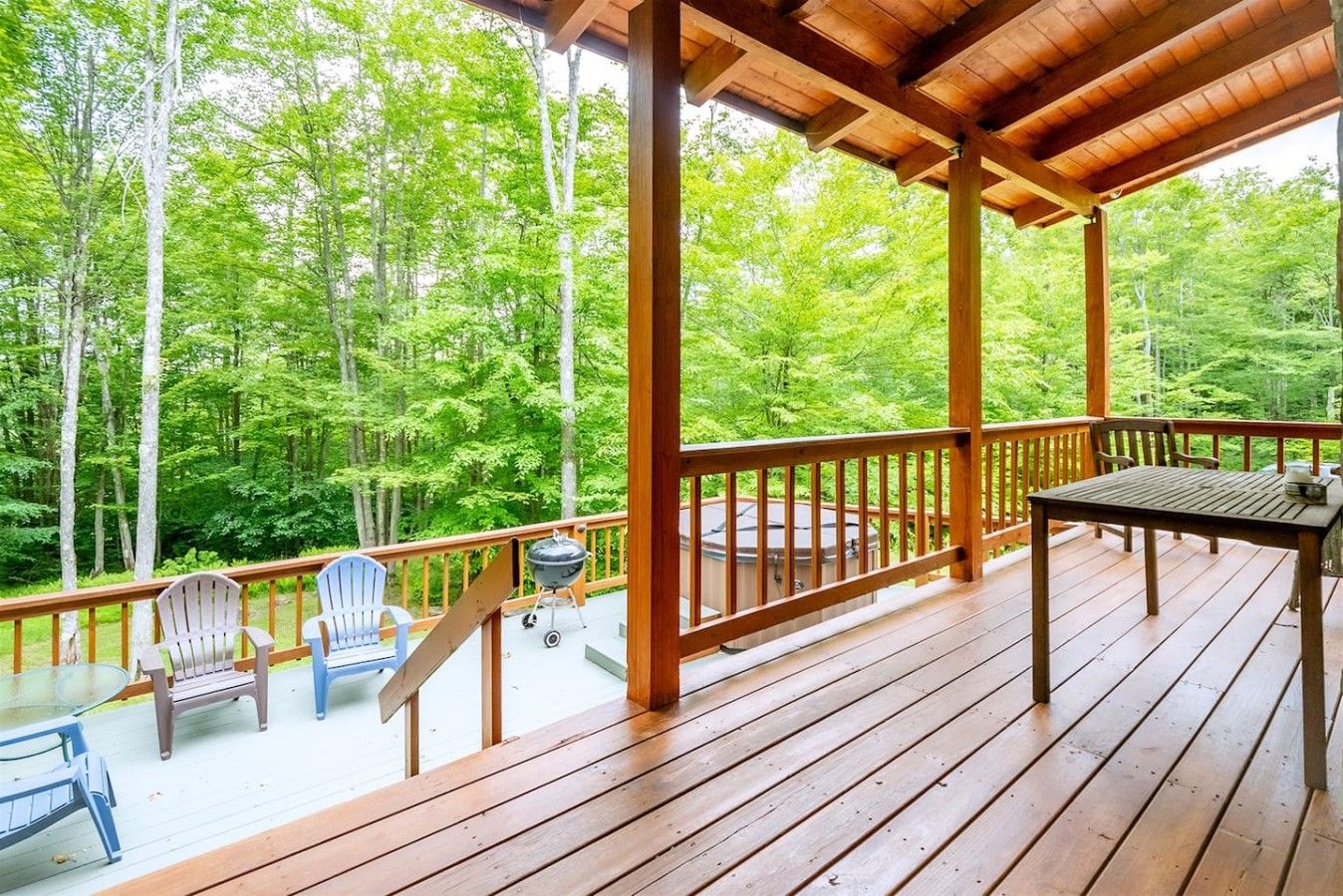 A wooden deck with a table and chairs, overlooking a forested area.