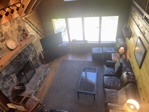 A cozy living room with a stone fireplace, a flat-screen TV, a glass coffee table, and a leather sofa.