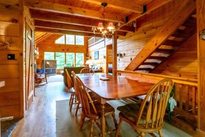 A wooden cabin interior with a dining table, chairs, a staircase, and a chandelier.