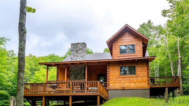 Uma cabana de madeira com chaminé de pedra, um deck e um alpendre.