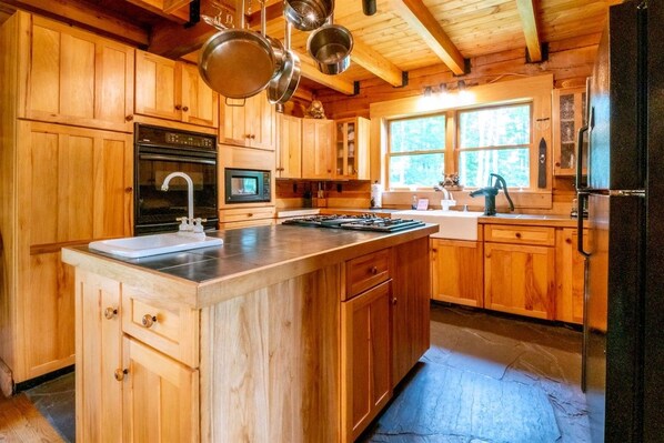 A wooden cabin-style kitchen with a central island, stainless steel appliances, and a large window.