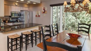 Une cuisine moderne dotée d’appareils électroménagers en acier inoxydable, un coin repas avec une table et des chaises en bois, et une grande fenêtre offrant une vue sur les arbres.