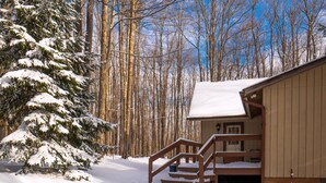 A wooden cabin with a snow-covered deck and stairs leading to a door.