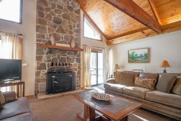 A cozy living room with a stone fireplace, a television, a sofa, and a painting on the wall.