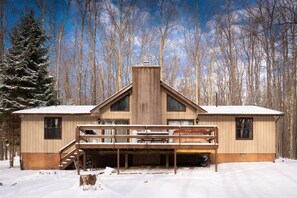 A wooden cabin with a deck, surrounded by snow and trees.