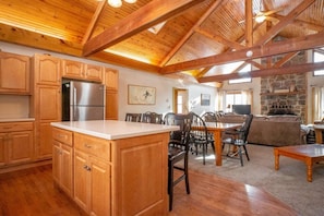 A spacious kitchen with wooden cabinets and a large island, a dining area with chairs, and a stone fireplace.