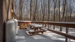 A wooden deck with a picnic table and benches, surrounded by a snowy forest.