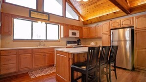 A kitchen with wooden cabinets, a stainless steel refrigerator, a microwave, and a large window.