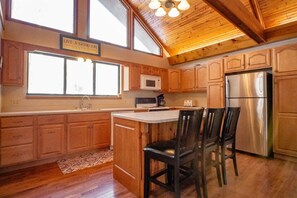 A kitchen with wooden cabinets, a stainless steel refrigerator, a microwave, and a dining area with chairs.