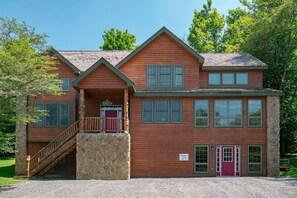 A two-story log cabin with a stone foundation, a porch with a wooden staircase, and a red door. - Hawthorne Lodge - Walk to Slopes, Air Conditioning (Davis)