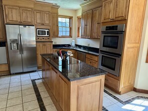 A kitchen with wooden cabinets, stainless steel appliances, a granite countertop, and a tiled floor.