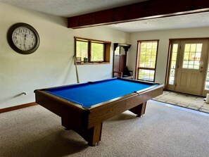 A pool table in a room with a clock on the wall, windows, and a door.