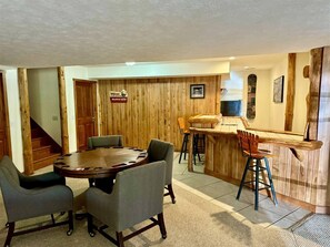 A wooden interior with a round table and chairs, a bar area, and a staircase.