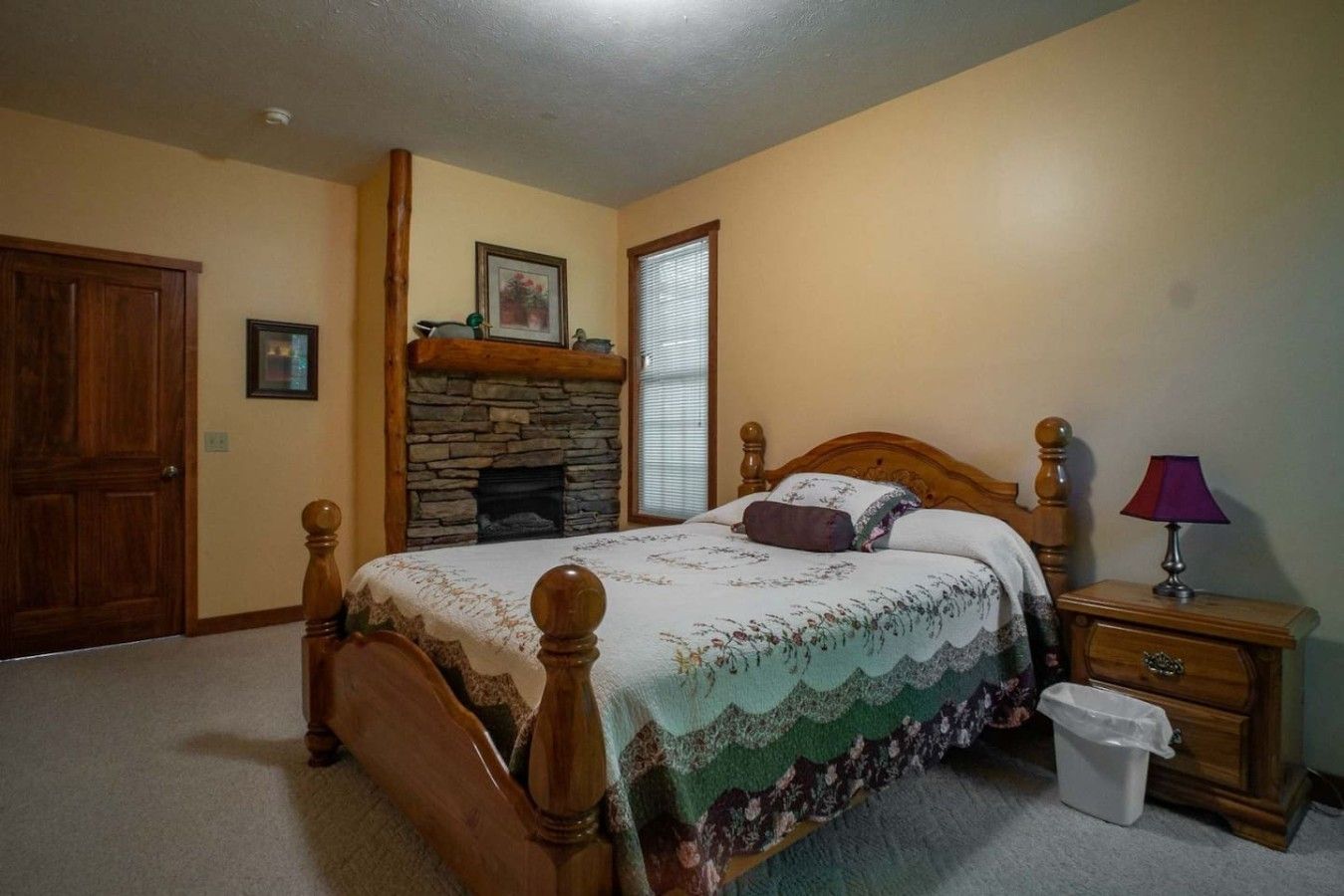 Une chambre à coucher avec un lit en bois, une cheminée en pierre, une table de chevet avec une lampe et une porte.