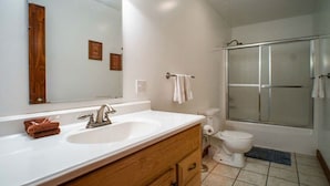 A bathroom with a white sink, wooden vanity, a mirror, a toilet, and a glass shower enclosure.