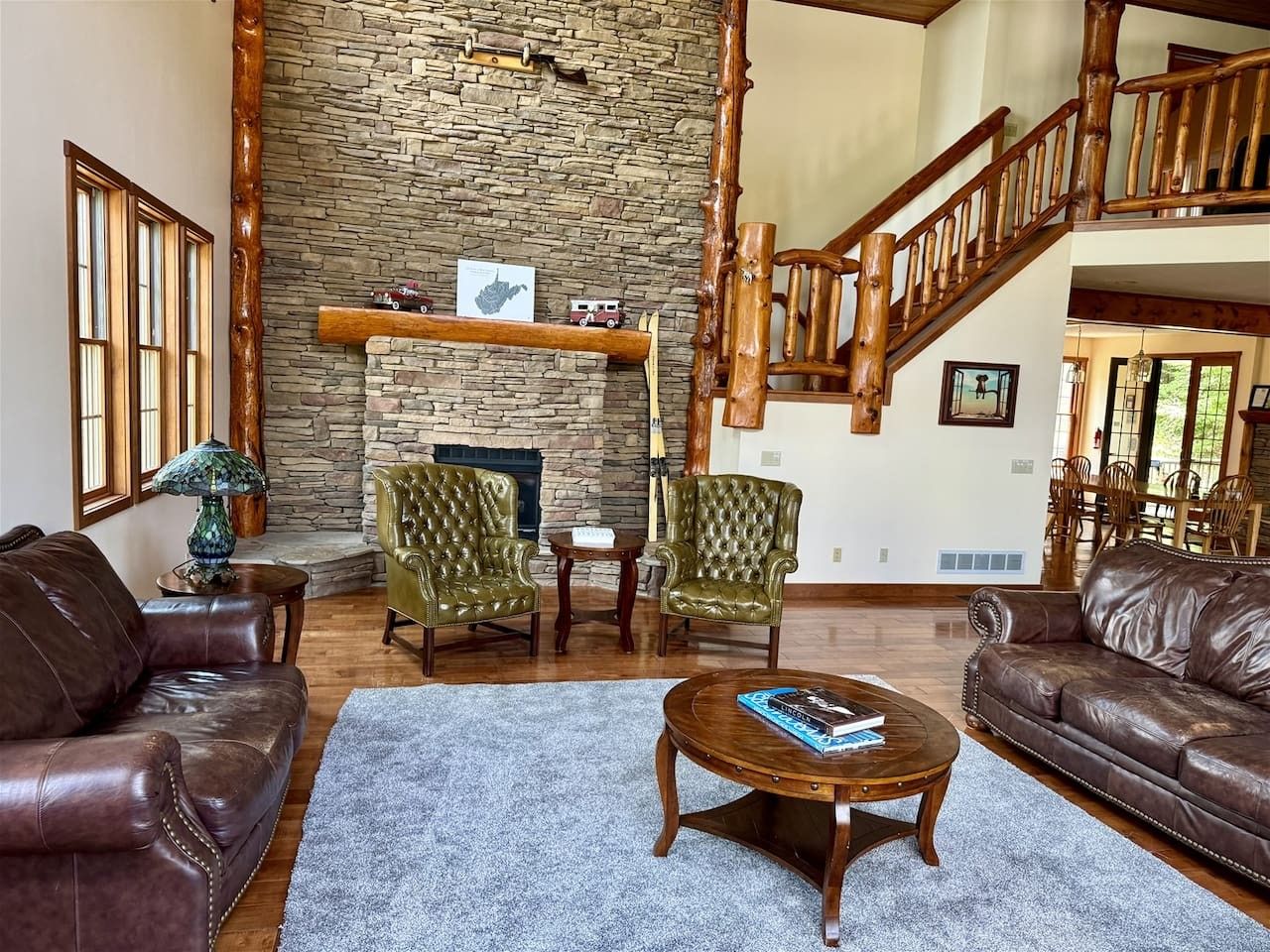 A spacious living room with a stone fireplace, leather sofas, and a wooden staircase.