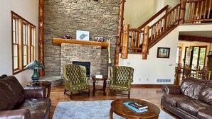 A spacious living room with a stone fireplace, leather sofas, and a wooden staircase.
