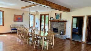 A dining area with a wooden table and chairs, a stone fireplace, and a large window.