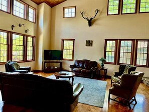 A spacious living room with a fireplace, leather sofas, a television, and a mounted deer head.